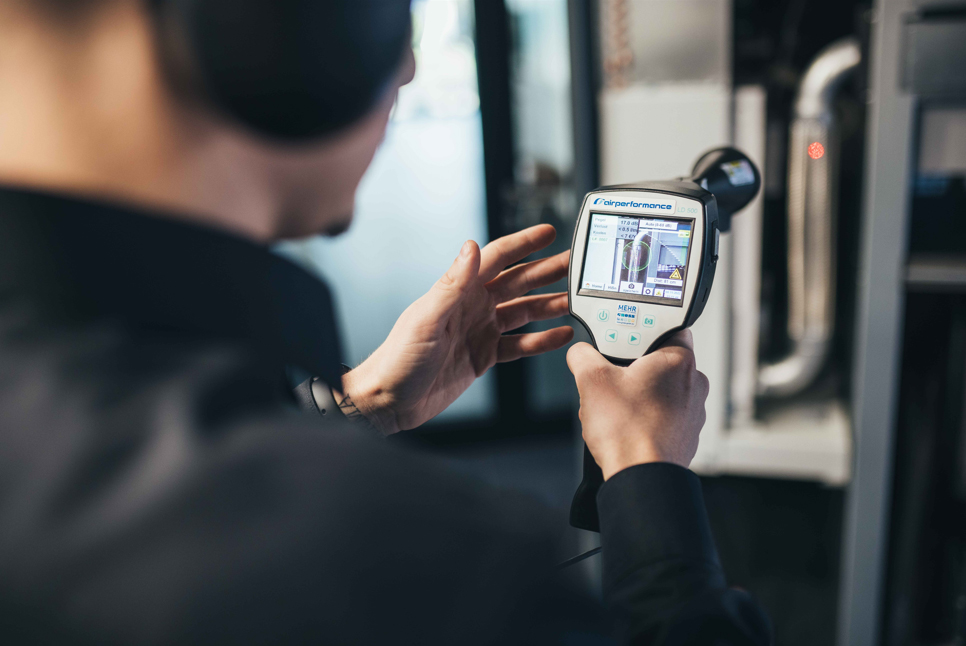 Servicetechniker bei der Leckageortung an einer Druckluftanlage mit Messgerät– Airgroup Partner